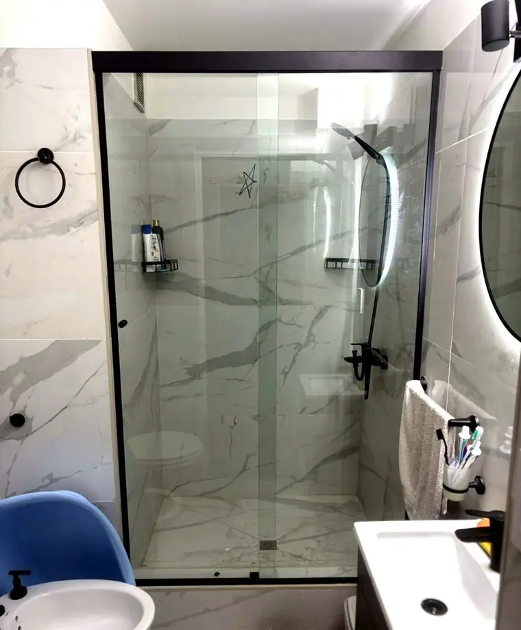 Baño remodelado con porcelanato símil mármol y mampara de vidrio con perfilería negra