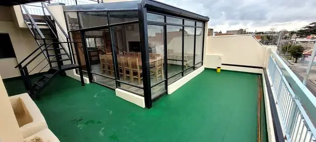 Terraza con quincho vidriado, piso impermeabilizado en verde y escalera metálica
